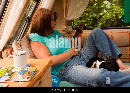 Frau saß in ihrem Wohnwagen eine Kindle e-Reader e-Book mit ihrem Jack Russell Hund auf dem Schoß zusammengerollt zu lesen. Stockfoto