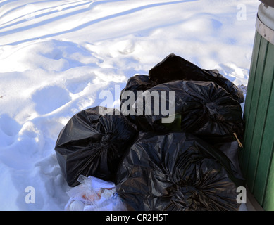 Schwarze Müllsäcke auf Schnee neben Müllcontainer im Winter. Stockfoto