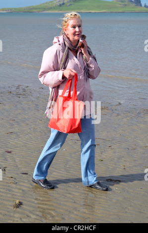 Frau geht mit einer kleinen roten Tasche am Strand Stockfoto