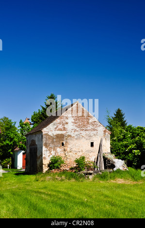 vertrocknete alte Backsteinhaus in eine saftig grüne Wiese an einem Sommertag mit einer Kapelle im Hintergrund Stockfoto