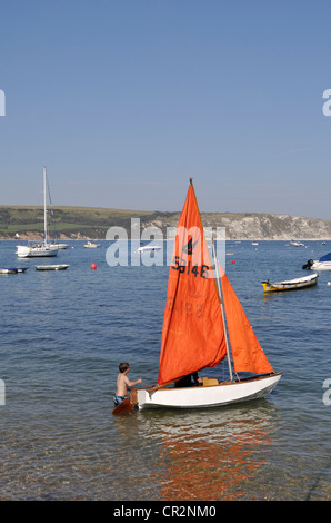 Ein kleiner Junge hilft seinem Vater mit einer Jolle bei Swanage, Dorset. Im Hintergrund sind die Kreidefelsen von Ballard Down. Stockfoto