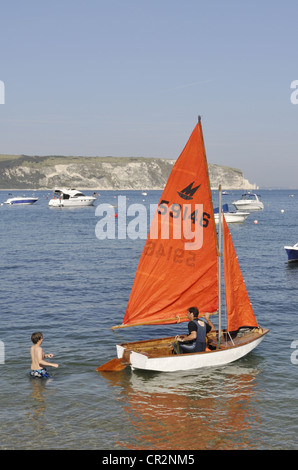 Ein kleiner Junge hilft seinem Vater mit einer Jolle bei Swanage, Dorset. Im Hintergrund sind die Kreidefelsen von Ballard Down. Stockfoto