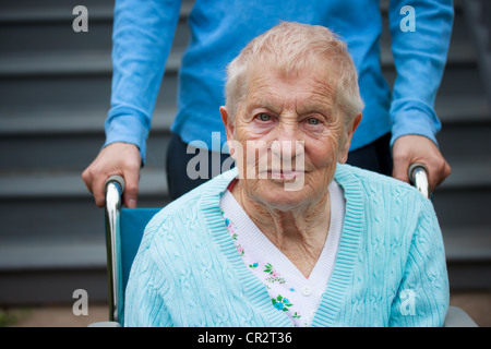 Senior-Frau im Rollstuhl mit Assistent hinter ihr. Stockfoto