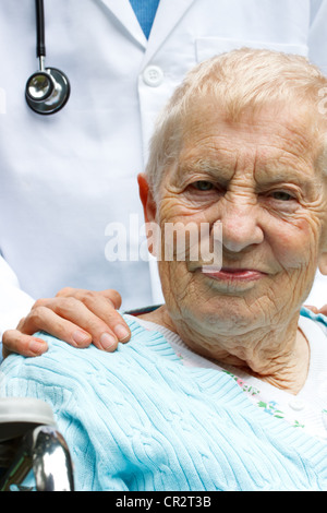 Senior-Frau im Rollstuhl mit Arzt hinter ihr Stockfoto