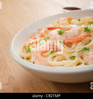 Eine Schüssel mit leckeren cremigen Alfredo Sauce mit Fettucine, Garnelen oder Krabben und eine Prise Petersilie auf einem Holztisch. Stockfoto