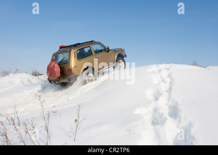 Lada Niva SUV Jeep fährt auf dem schneebedeckten Hügel. Das Schild an der Heckscheibe ist nicht urheberrechtlich geschützt. Stockfoto