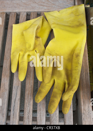 Schmutzig gelb Kunststoff-Handschuhe, die für die Gartenarbeit Verlegung auf einem Holzstuhl Garten verwendet wurde. Stockfoto