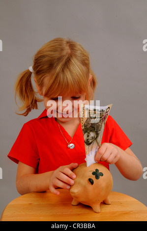 Kleines Mädchen, 5 Jahre, Geld in ein Sparschwein Stockfoto