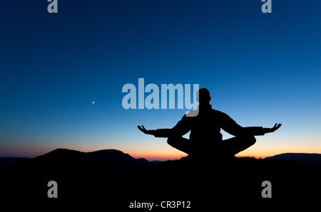 Ein Mann ist Meditation, im Gebet auf dem Gipfel eines Berges als die Sonnenuntergänge. Stockfoto