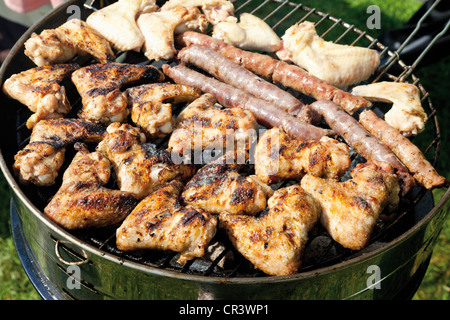 Chicken Wings und Würstchen auf einem Holzkohlegrill Stockfoto