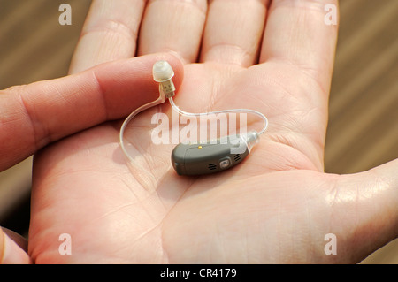 Moderne kleine Hörgerät in der Handfläche einer Frau, Schwerhörigkeit Stockfoto