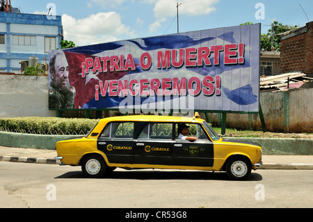 Gestreckte Lada-Taxi vor eine Werbetafel mit politischer Propaganda darauf, Fidel Castro, Socialismo o muerte Stockfoto