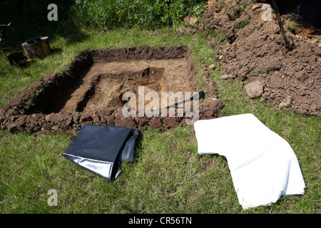 Graben ein Loch, um einen Teich im Garten im Vereinigten Königreich mit Teichfolie und Schutzfolie zu errichten Stockfoto