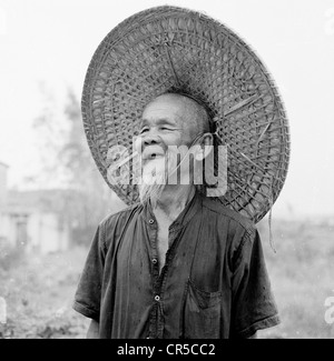 Hong Kong, 1950er Jahre. Eine ältere männliche chinesische Arbeiter in traditioneller Tracht tragen eine große Runde Wicker konische oder einen Kuli Hut. Stockfoto