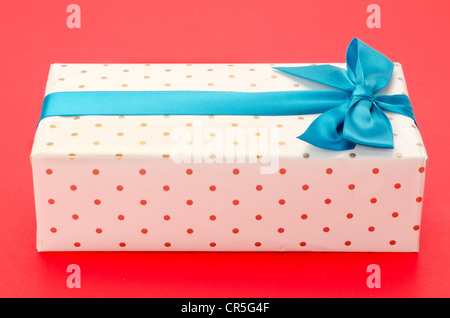 Verpackte Geschenkbox mit einem blauen Band und Bogen - gedreht im Studio mit einem roten Hintergrund Stockfoto