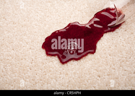 Rotwein aus einem Glas auf ein Licht verschütten farbigen Teppich. Stockfoto