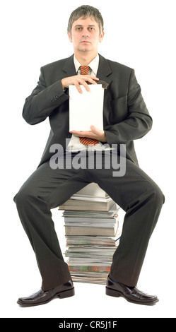 Geschäftsmann, sitzen auf gestapelten Büchern präsentiert leeren weißen Hardcover-Buch Stockfoto