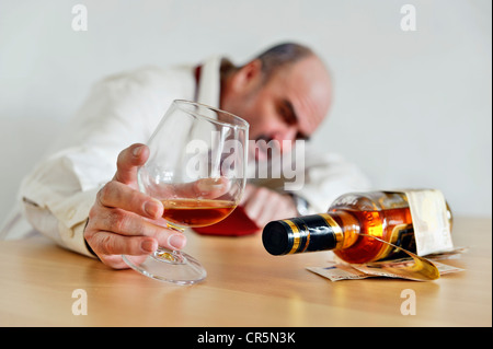 Alkohol-Süchtigen mit einem Cognac-Glas, mit einer Flasche Alkohol an einem Tisch sitzen Stockfoto