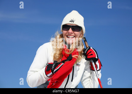 Junge Frau, ca. 25 Jahre, trug eine helle Jacke, Mütze, dunkle Sonnenbrille und ein rotes Halstuch, vor blauem Himmel Stockfoto