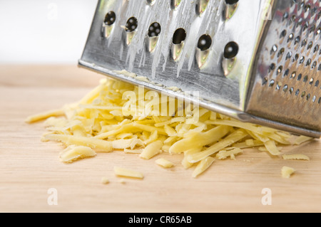 Geriebenen Käse mit Reibe auf hölzernen Schneidebrett vor weißem Hintergrund Stockfoto