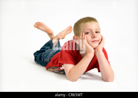 Studio Bild des kaukasischen 8 Jahre alter Junge liegend am Boden, stützte sich auf Arme auf weißem Hintergrund Stockfoto