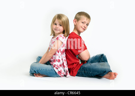Zwei kaukasischen Kinder, Bruder und Schwester saß Rücken an Rücken lächelnd (7 Jahre altes Mädchen und 8 Jahre alt) auf einem weißen Hintergrund Stockfoto