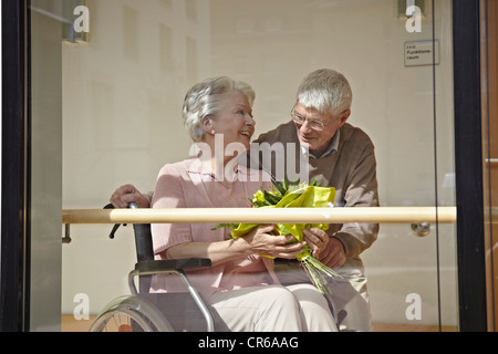 Deutschland, Köln, Senior Frau im Rollstuhl mit Blumenstrauß, Mann, Lächeln Stockfoto