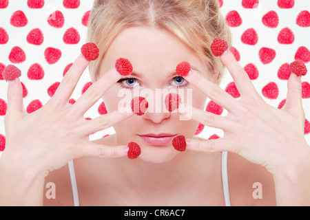 Junge Frau mit Himbeeren auf ihren Fingerspitzen Stockfoto