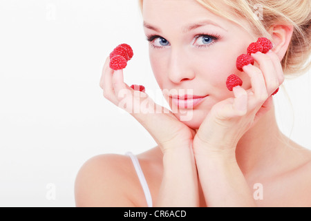 Junge Frau mit Himbeeren auf ihren Fingerspitzen, Porträt Stockfoto