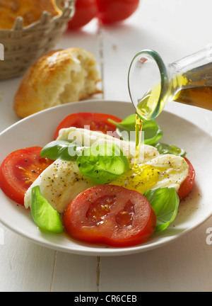 Olivenöl Gießen auf Caprese-Salat auf Teller, Nahaufnahme Stockfoto