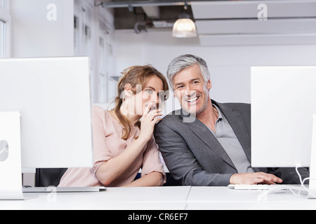 Deutschland, Bayern, München, Frau des Mannes Ohr im Büro zu flüstern Stockfoto