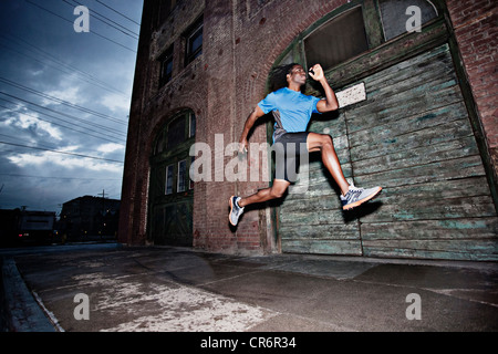 Männlicher Athlet läuft auf Bürgersteig Stockfoto
