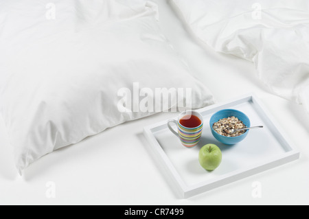 Tablett mit Tee, Apfel und Müsli auf Bett zum Frühstück Stockfoto