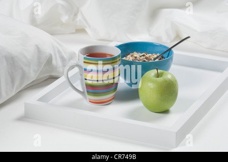 Tablett mit Tee, Apfel und Müsli auf Bett zum Frühstück, Nahaufnahme Stockfoto