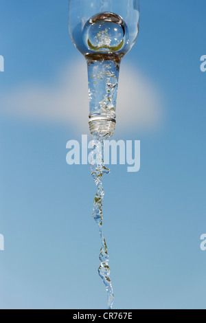 Gießen Wasser aus einer Glasflasche vor blauem Himmel Stockfoto