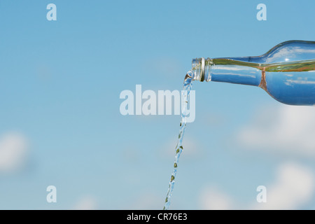 Gießen Wasser aus einer Glasflasche vor blauem Himmel Stockfoto