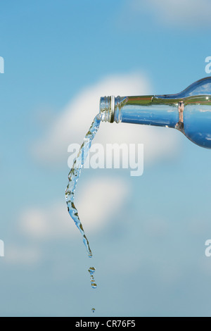 Gießen Wasser aus einer Glasflasche vor blauem Himmel Stockfoto