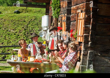 Österreich, Salzburger Land, Männer und Frauen sitzen auf Alm, Musiker anhören Stockfoto