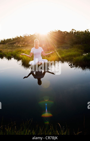 Österreich, Salzburger Land, junge Frau sitzt in der Nähe von Bergsee und Meditation zu tun Stockfoto