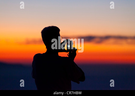 Mann ein Foto mit einem Handy oder einer kompakten Kamera, bei Sonnenuntergang Silhouette Stockfoto