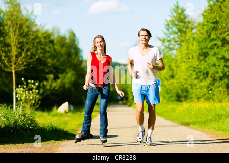 Junges Paar - Mann und Frau - macht Sport im Freien, er ist Joggen während sie Inlineskating ist Stockfoto