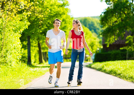 Junges Paar - Mann und Frau - macht Sport im Freien, er ist Joggen während sie Inlineskating ist Stockfoto