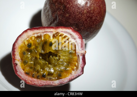 Passionsfrucht (Passiflora Edulis), einem ganzen und einer halbiert, auf einem weißen Teller Stockfoto