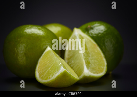 Limes (Citrus Latifolia) und Kalk Stücke auf einer dunklen Glasplatte Stockfoto