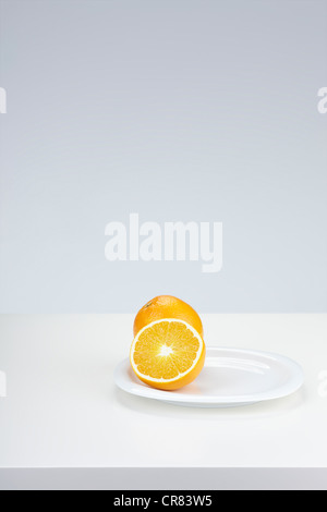 Zwei Orangen (Citrus Sinensis), eine ganze Frucht und einer halbierten Frucht, auf einem weißen Teller Stockfoto