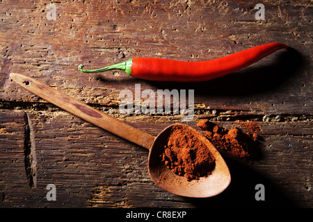 Chili-Pfeffer (Capsicum) mit einem Holzlöffel und Chilipulver auf einer rustikalen Holzoberfläche Stockfoto