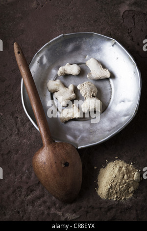 Ingwer (Zingiber Officinale) Wurzeln auf einem Zinn-Teller mit einem Holzlöffel und gemahlener Ingwer auf eine Steinoberfläche Stockfoto