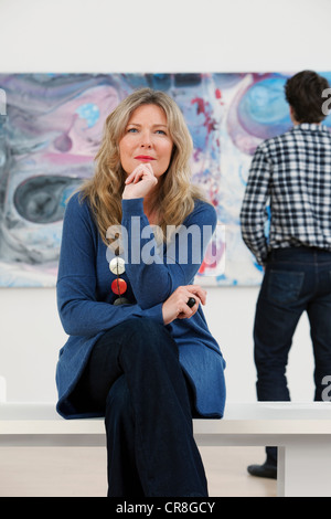 Mitte Erwachsene Frau sitzt vor Ölgemälde in Galerie Stockfoto