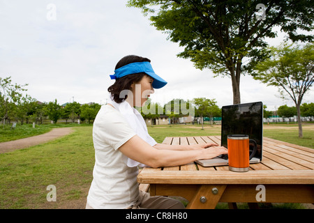 Frau mit Laptop auf Picknickbank im park Stockfoto