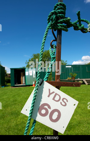 60 Yards Zeichen mit grünen Seil auf einem rostigen Metallstab mit grüner Gebäude hinter gebunden und gegen einen blauen Himmel Stockfoto